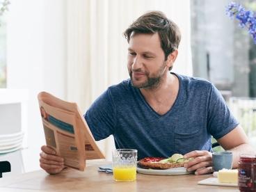 a man at a table reading a newspaper while eating breakfast